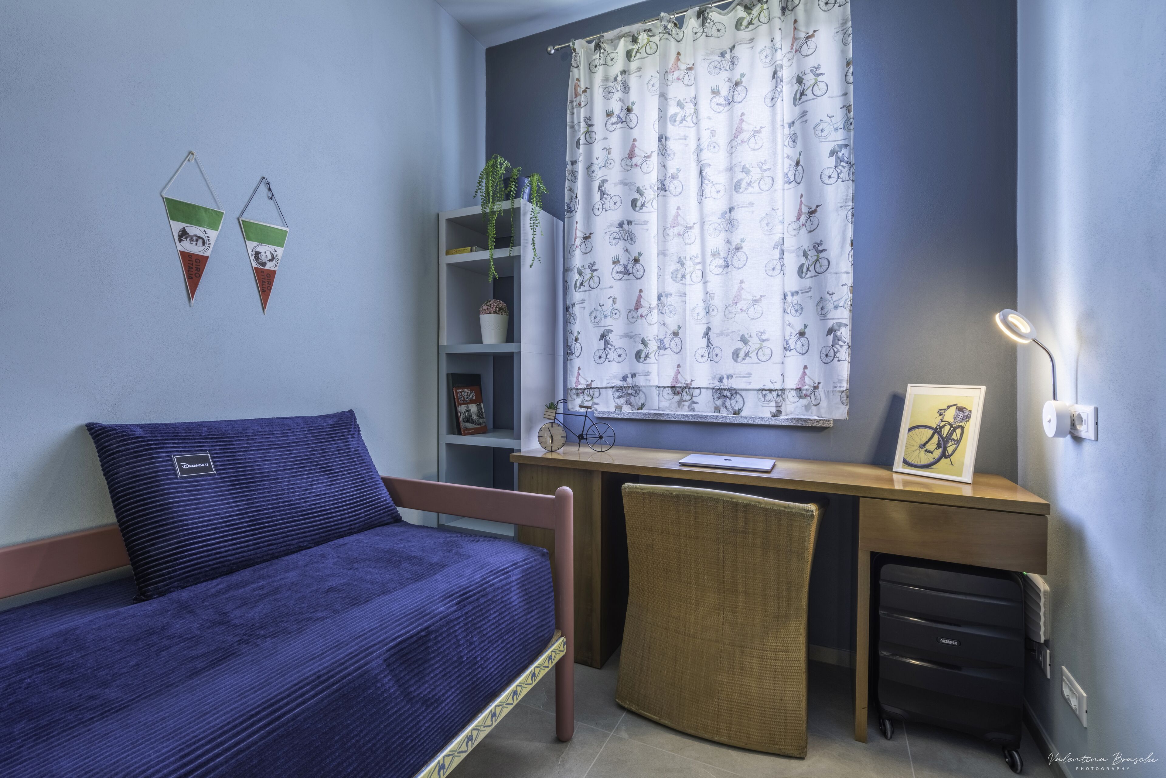 A bedroom with a bed, desk, chair, and a window with curtains.