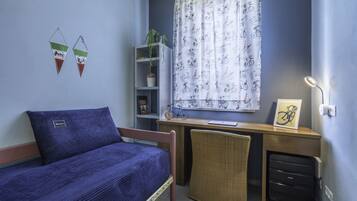 A bedroom with a bed, desk, chair, and a window with curtains.