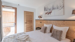 Une chambre avec une tête de lit en bois, un lit recouvert de linge de lit blanc, un tapis blanc moelleux et, au mur, un tableau représentant des cerfs dans une forêt enneigée.