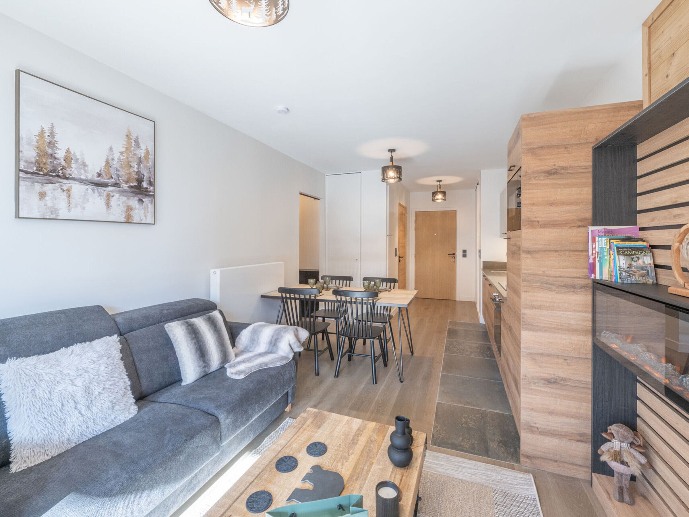 A modern living room with a grey sofa, a wooden coffee table, and a dining area with a wooden table and chairs.