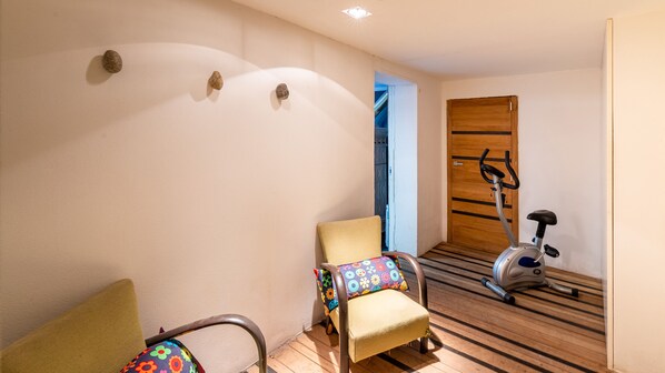 A hallway with a wooden floor, a chair with a colorful cushion, and an exercise bike.