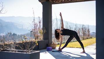 Una persona realiza una postura de yoga al aire libre, con vistas a montañas al fondo.