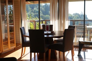 Zona pranzo con tavolo e sedie, un bicchiere di vino rosso e vista sugli alberi attraverso ampie finestre.