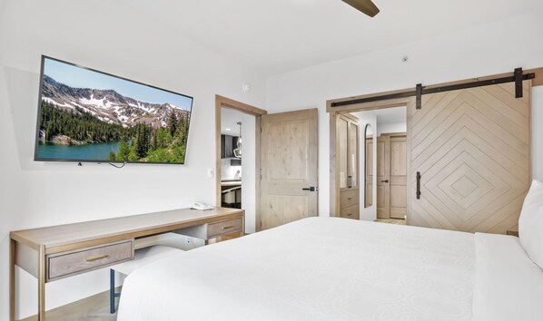 Un dormitorio con cama, escritorio, televisor y puerta corrediza.