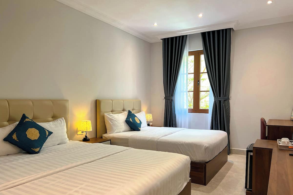 A hotel room with two beds, a wooden desk, and a window with curtains.