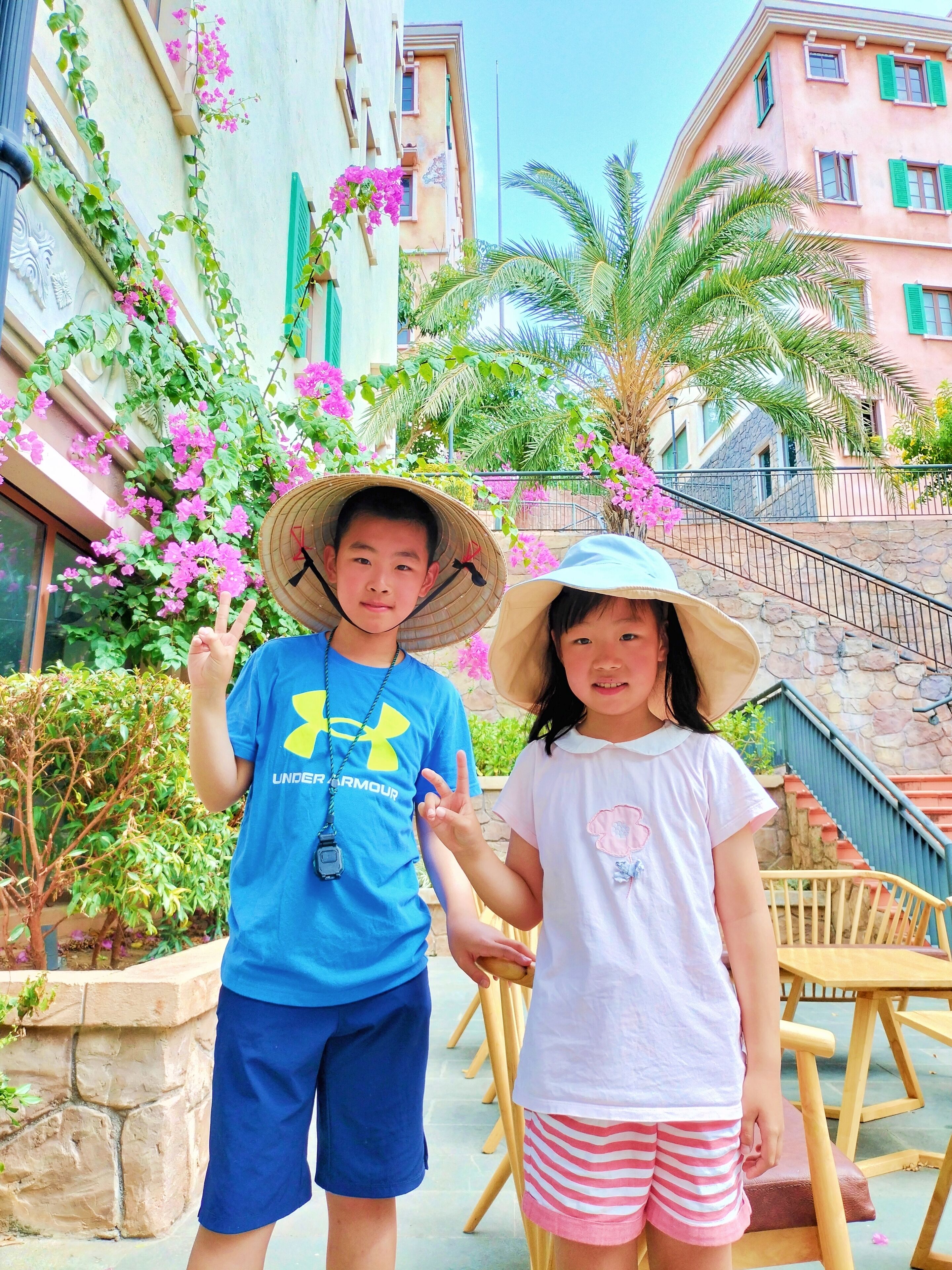 Two people standing in front of a building with a stone staircase and pink flowers.