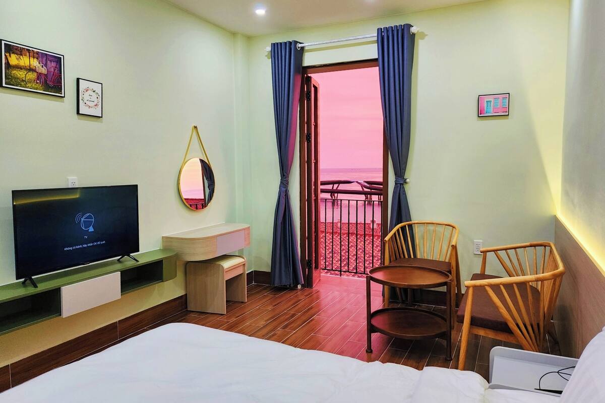 A hotel room with a bed, a TV, a desk, a chair, and a balcony with a view.