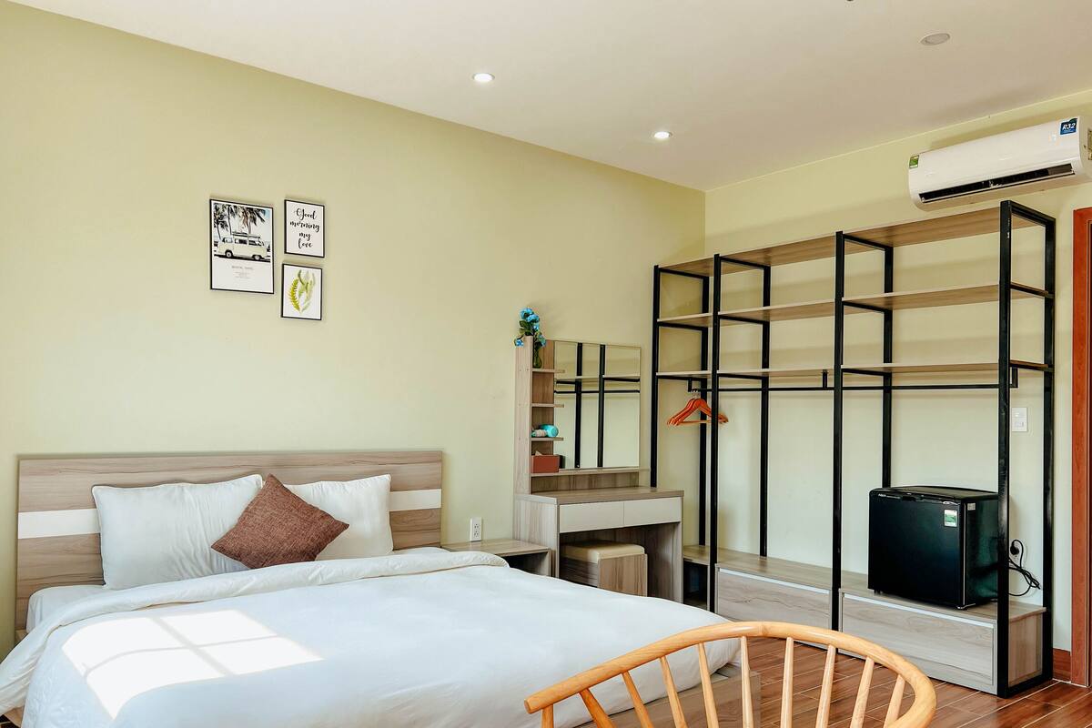 A bedroom with a bed, a wooden chair, a wardrobe with a mirror, and an air conditioner.