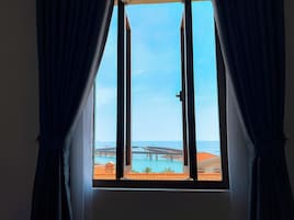 A window with curtains, a view of a coastal area with buildings and a bridge.