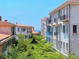 A row of colorful buildings with balconies, surrounded by lush greenery.