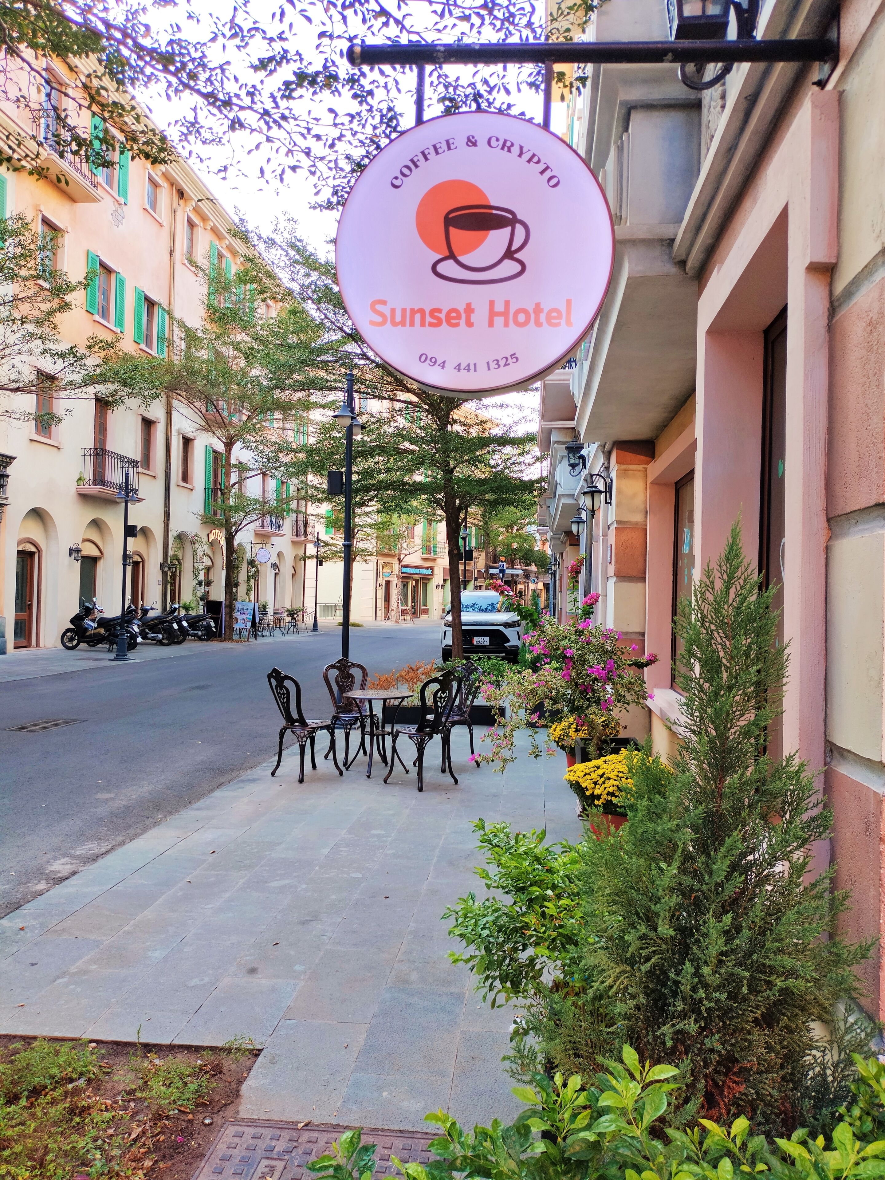 A street view of Sunset Hotel with outdoor seating and a signboard advertising coffee and crypto services.