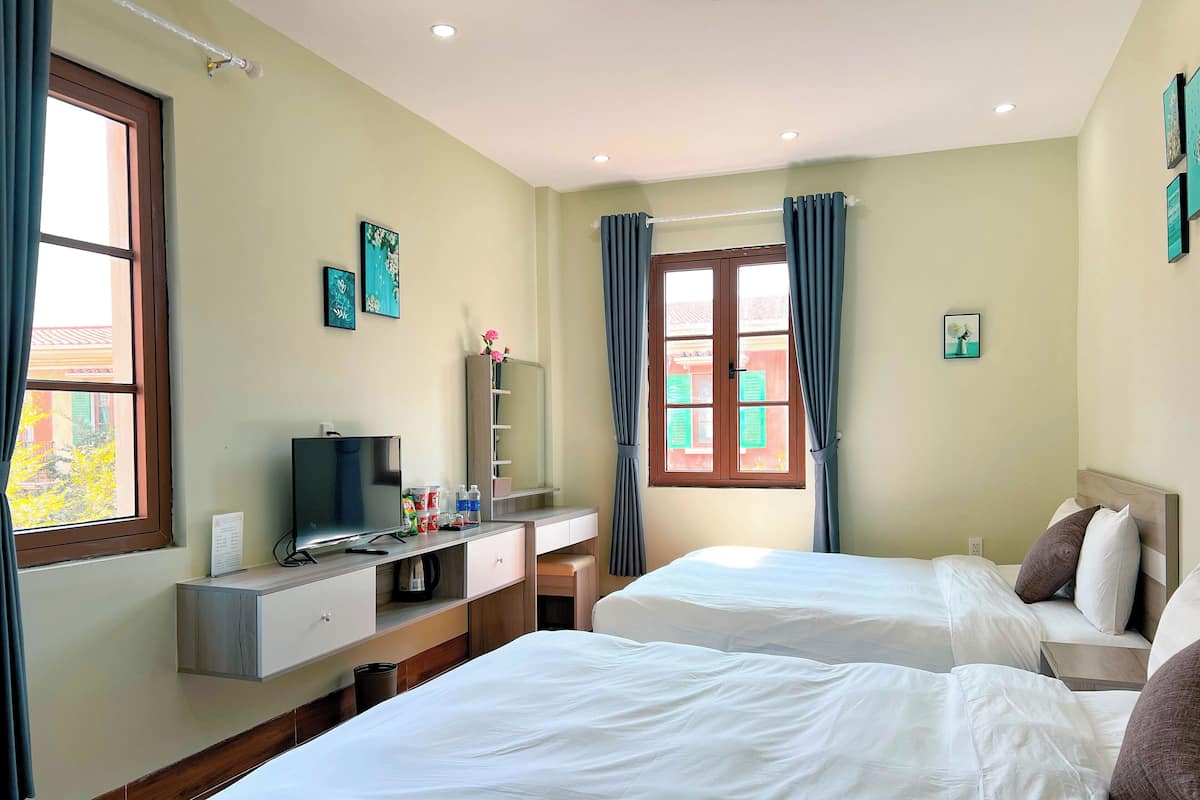 A hotel room with two beds, a TV, a desk, and a window with curtains.