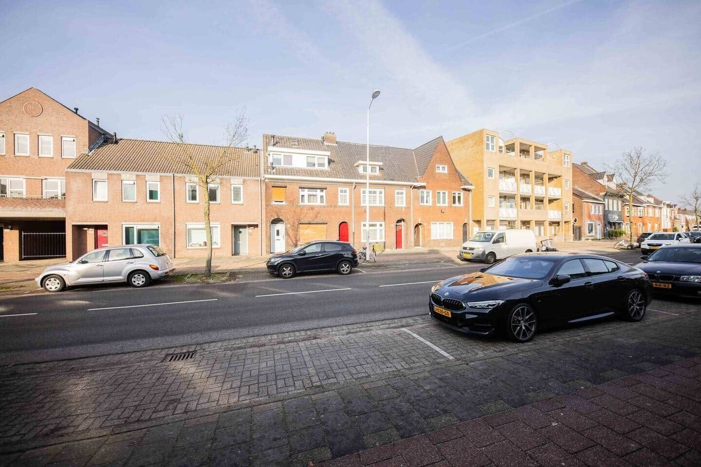 A residential street with houses, parked cars, and a clear sky.