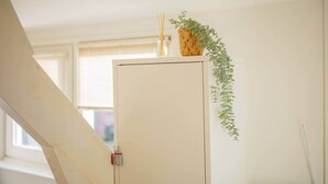 Um armário branco com um cadeado vermelho, uma cesta de vime com uma planta, e uma planta pendurada na parede.