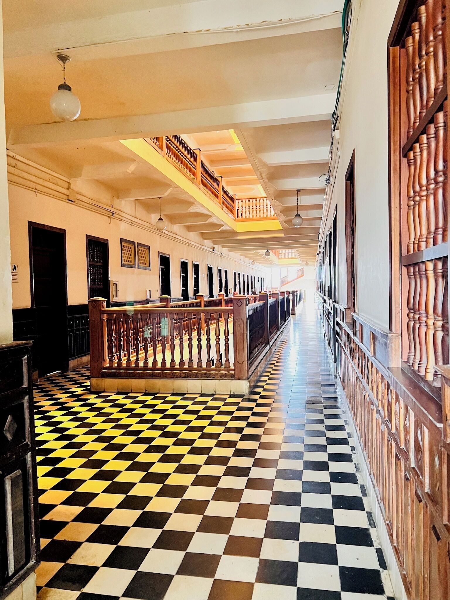 A hallway with a checkered floor, wooden railings, and a staircase leading to an upper level.