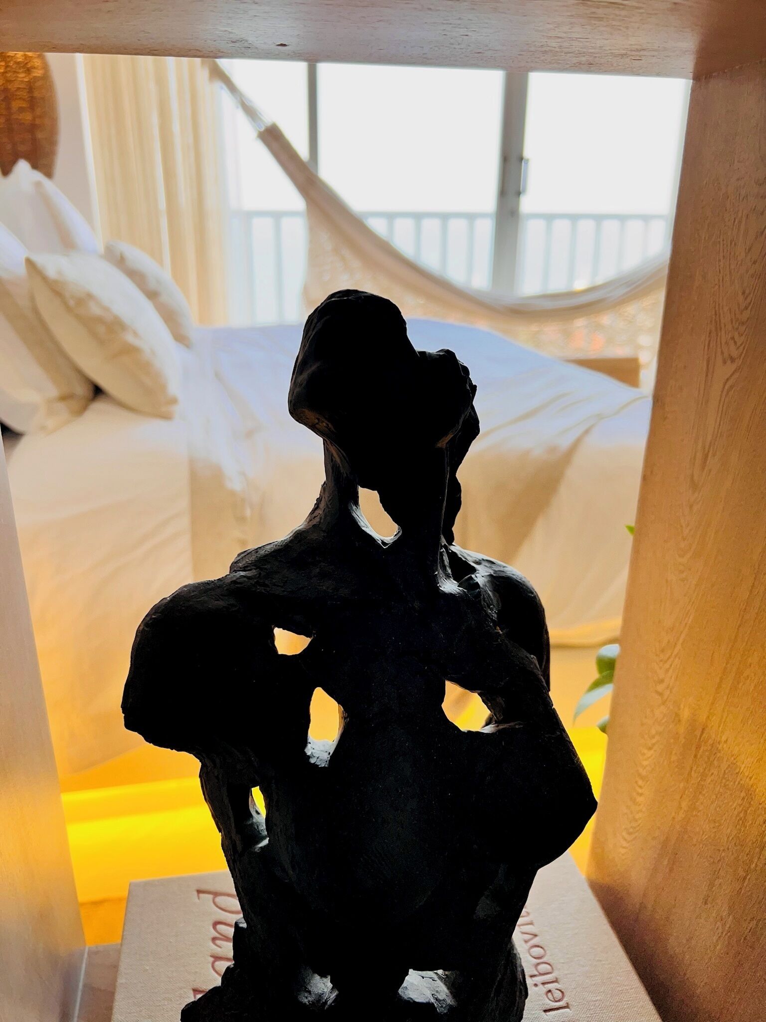 A sculpture on a table with a bed and curtains in the background.