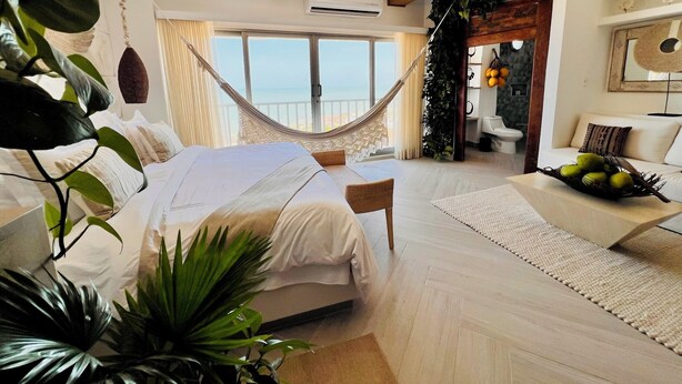 A spacious bedroom with a large bed, a hammock, and a view of the sea.