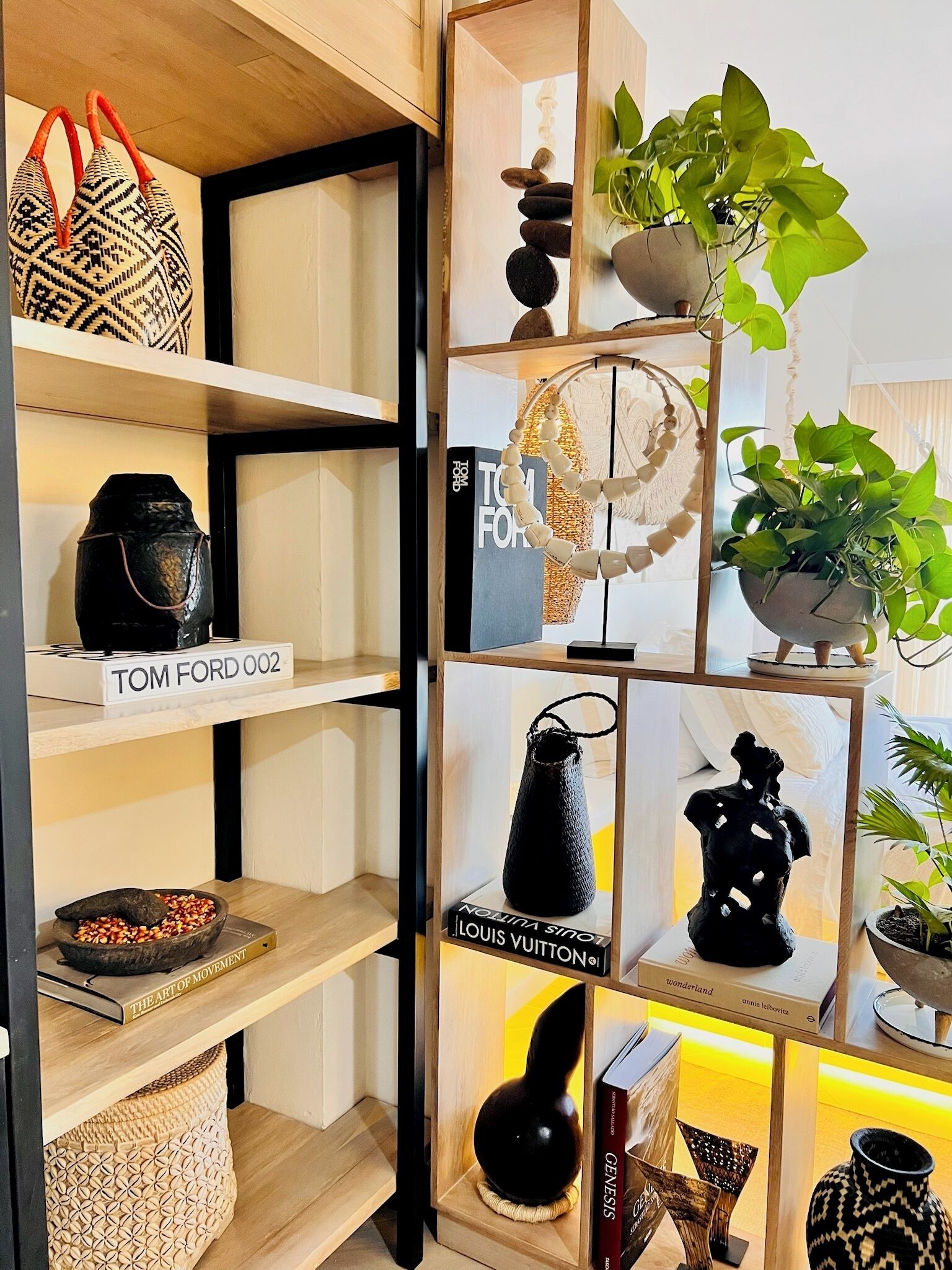 Une étagère bien organisée, agrémentée de divers objets décoratifs, notamment un sac tressé, un livre intitulé « TOM FORD 002 » et une plante en pot.