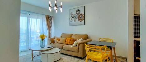 A modern living room with a sofa, a dining table with chairs, a round coffee table, and a chandelier.