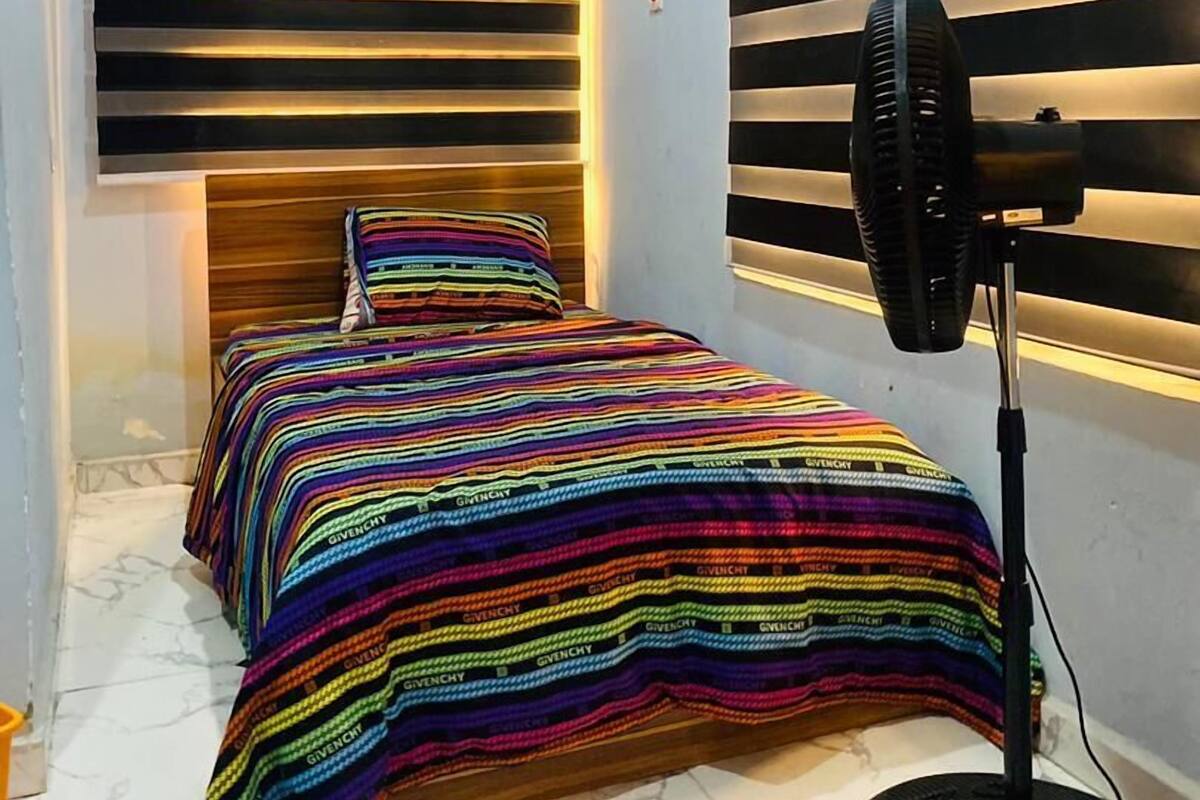 Une chambre à coucher avec un lit, un ventilateur et une fenêtre équipée de stores horizontaux.