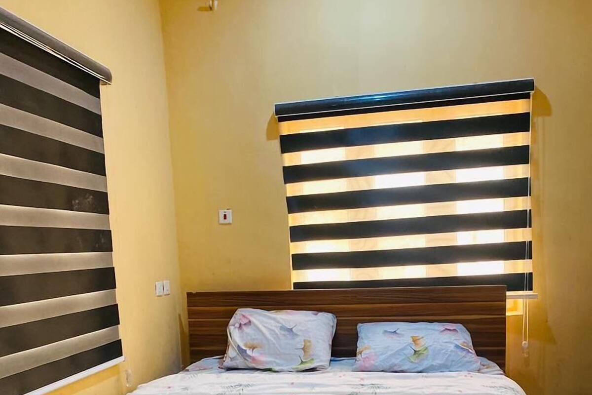 Une chambre à coucher avec un lit, une tête de lit en bois et une fenêtre avec des stores.