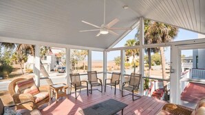 Un espace extérieur abrité, doté d’un ventilateur de plafond, de meubles en osier et offrant une vue sur la plage.