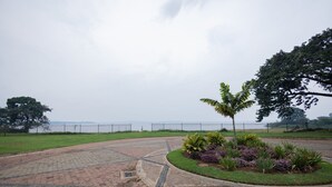 A paved area with a circular garden bed, a palm tree, and a fence. - Lake Victoria View 1 Bedroom Apartment Entebbe (Entebbe)