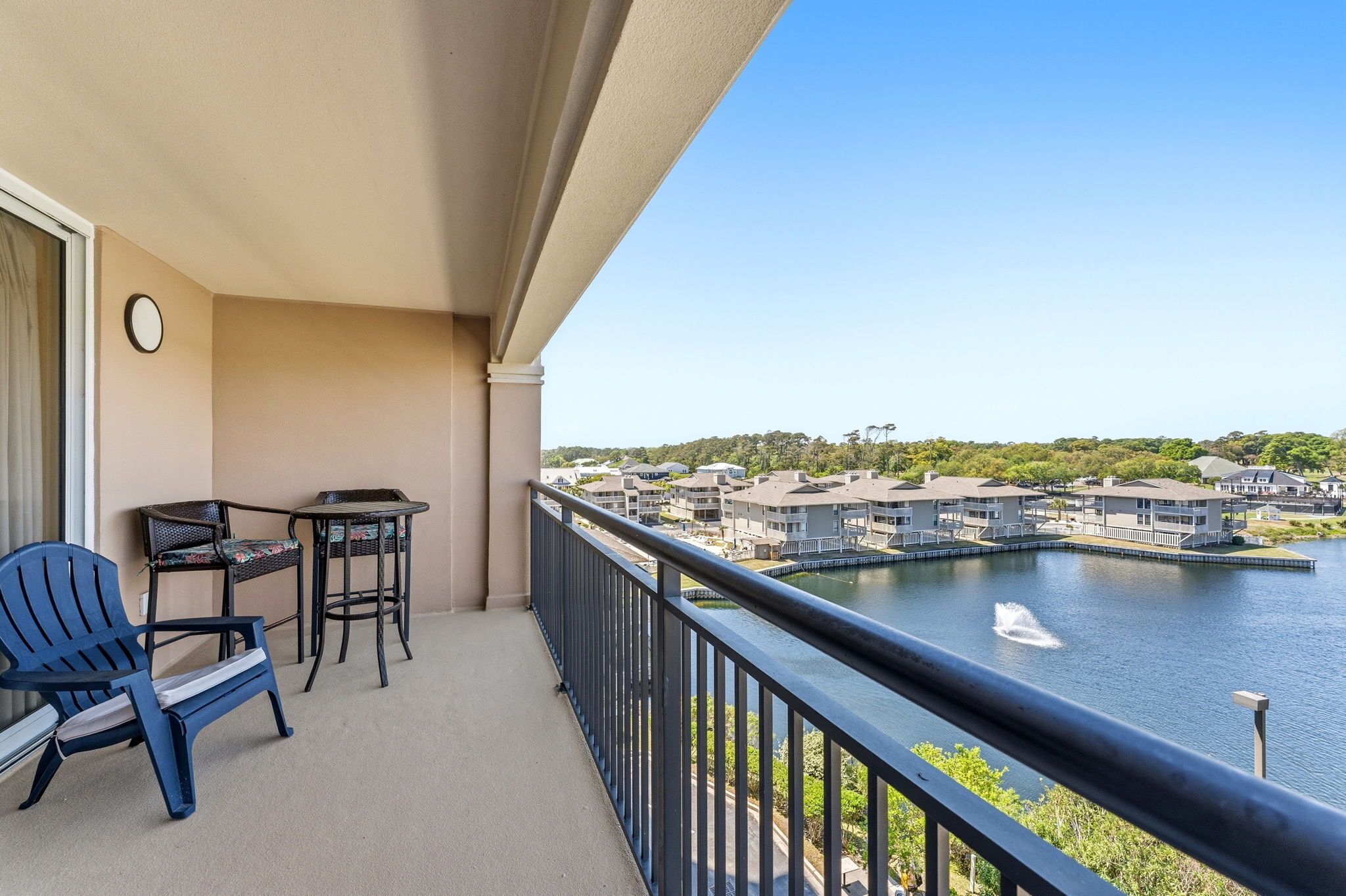 Ein Balkon mit Stuhl, Tisch und Blick auf einen See mit Gebäuden im Hintergrund.