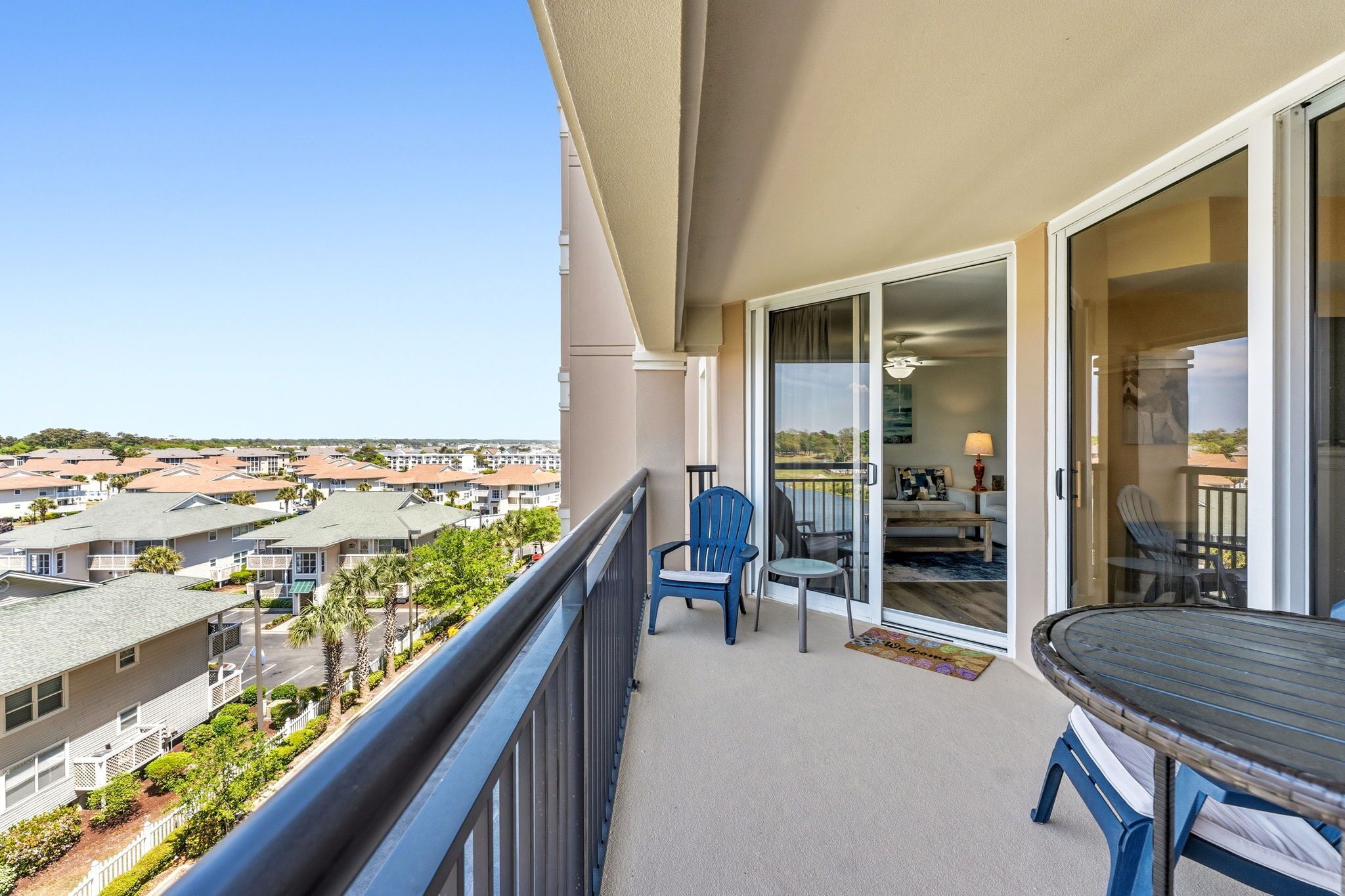 A balcony with a table and chairs, a sliding glass door leading to a living area, and a view of neighboring houses.