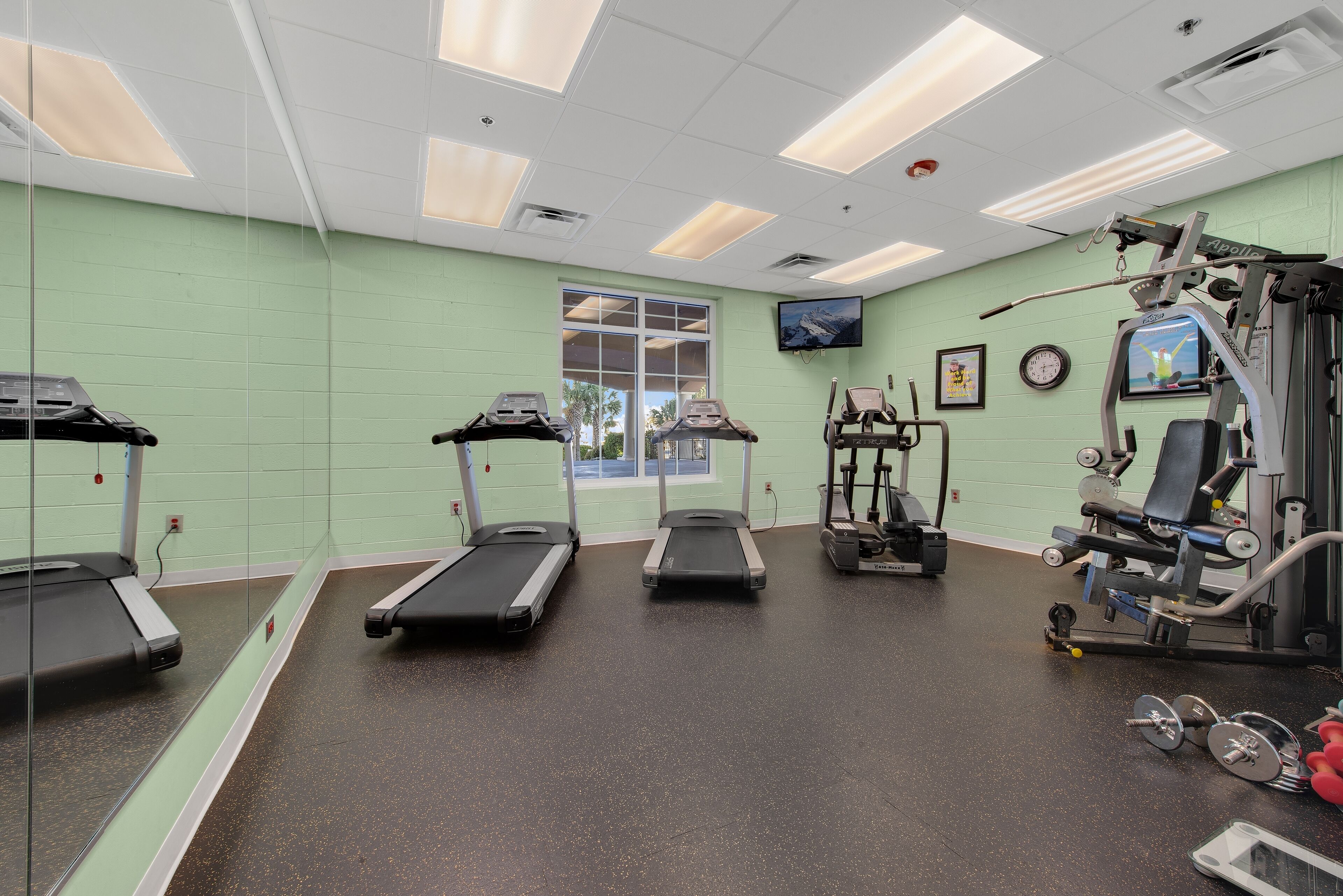 A gym with treadmills, a weight machine, and a television on the wall.