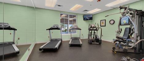 A gym with treadmills, a weight machine, and a television on the wall.