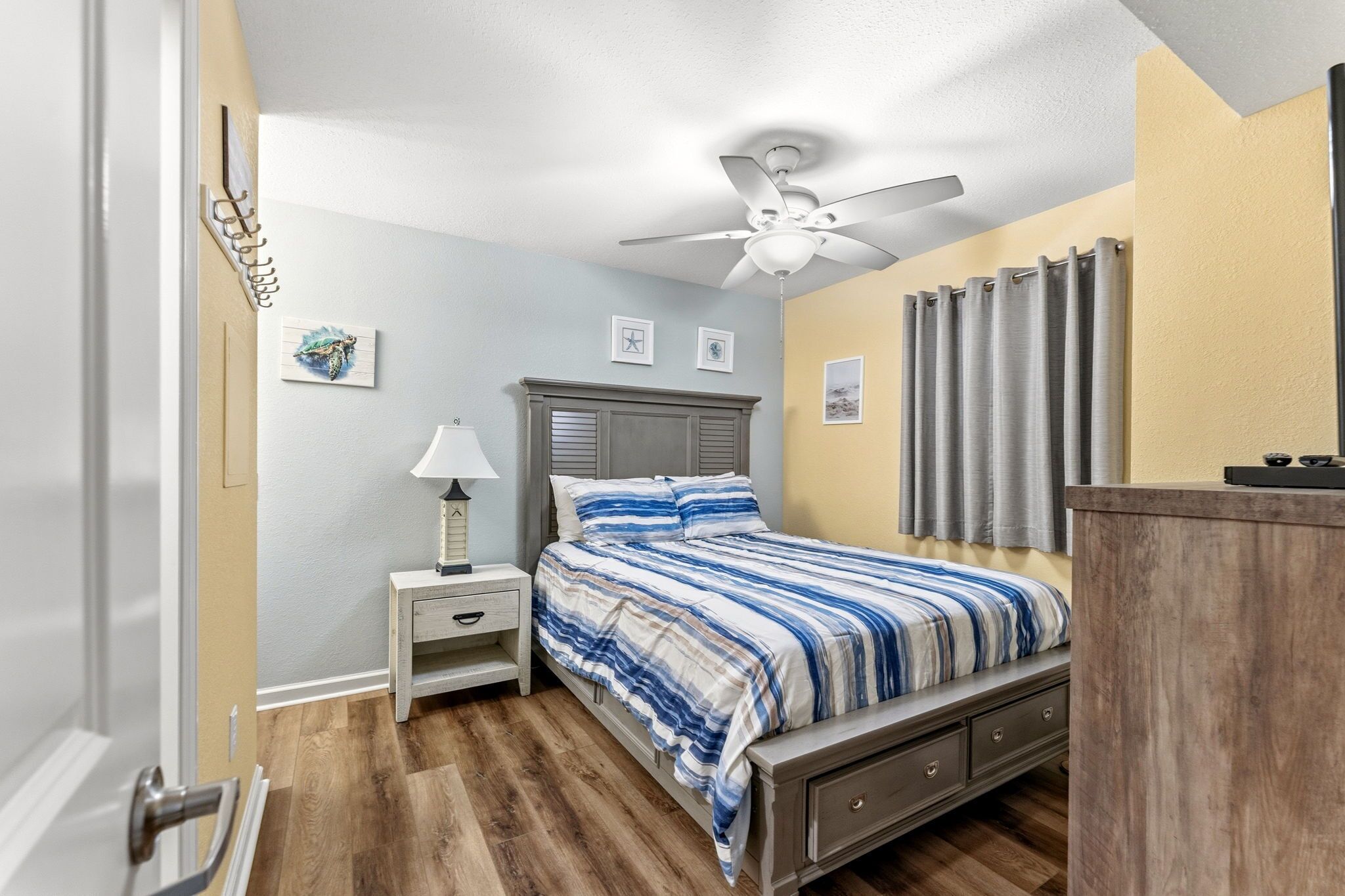 Ein Schlafzimmer mit Bett, Nachttisch, Lampe, Deckenventilator und Kommode.