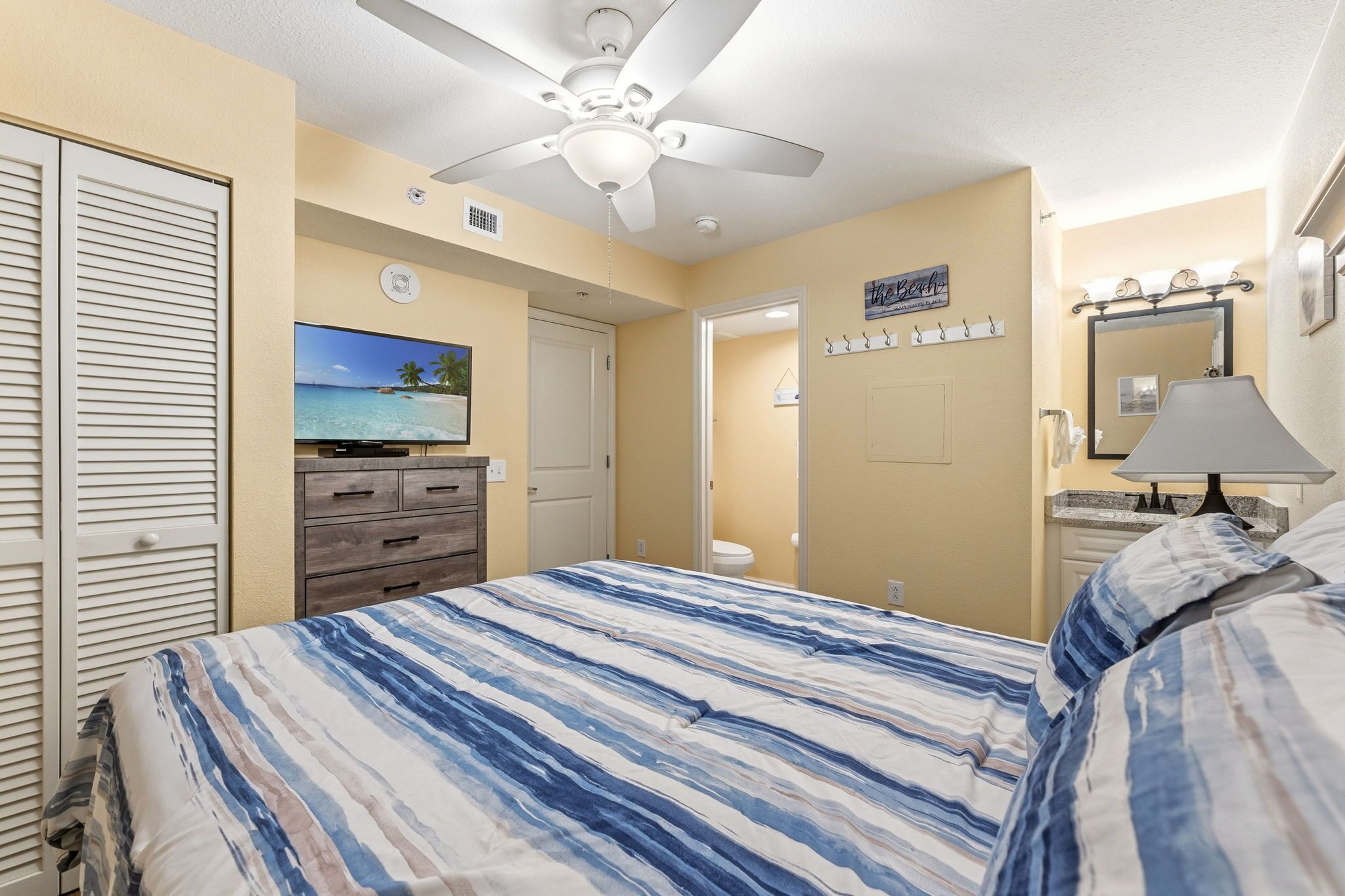Un dormitorio con cama, ventilador de techo, televisor, puerta de baño y espejo.