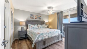 A bedroom with a bed, nightstands, a ceiling fan, and a window with curtains. - Spacious 2nd row condo, great amenities + Free Attraction Tickets! (North Myrtle Beach)