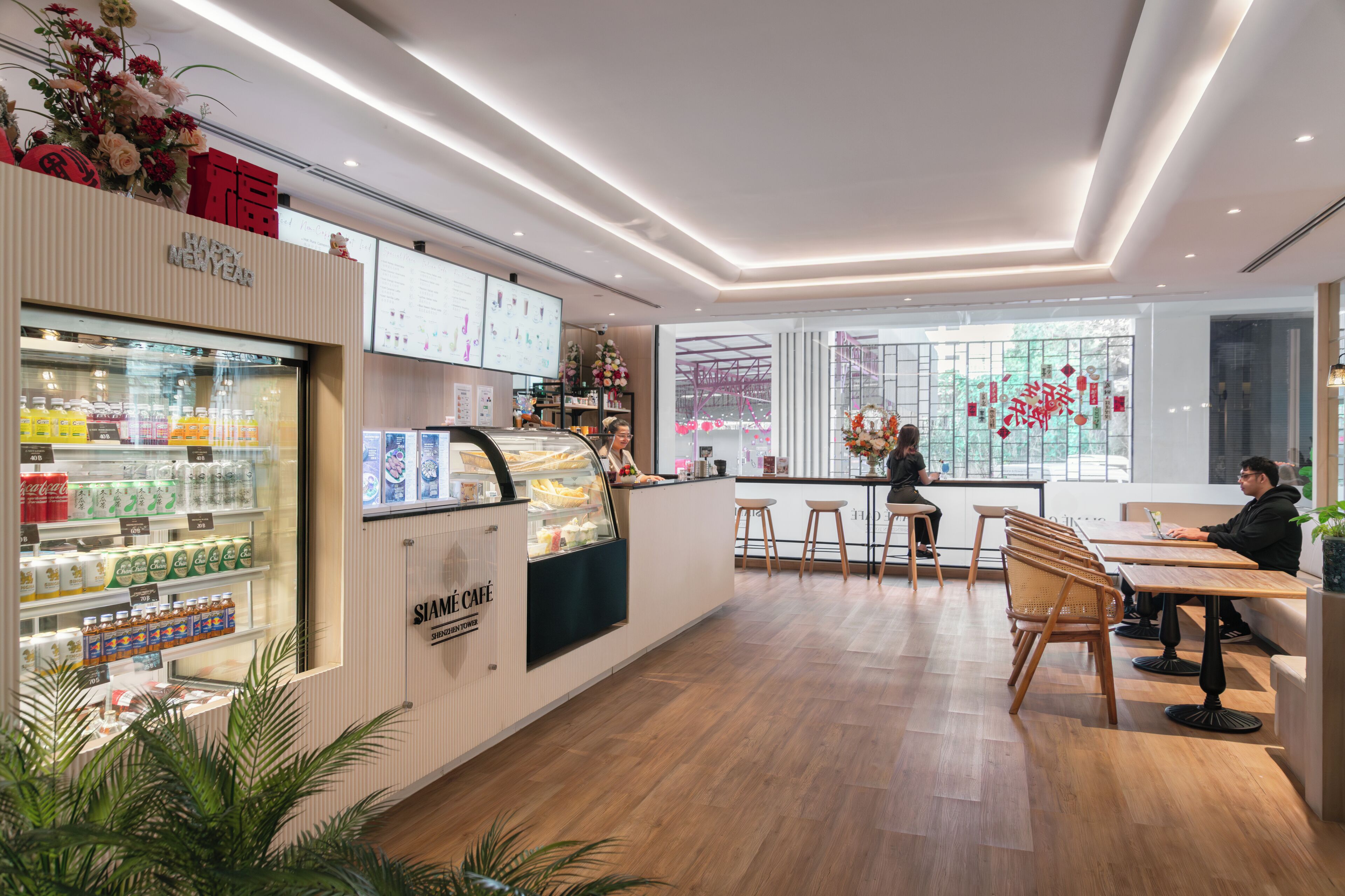A modern café with a wooden floor, a refrigerated display case, and a seating area with tables and chairs.