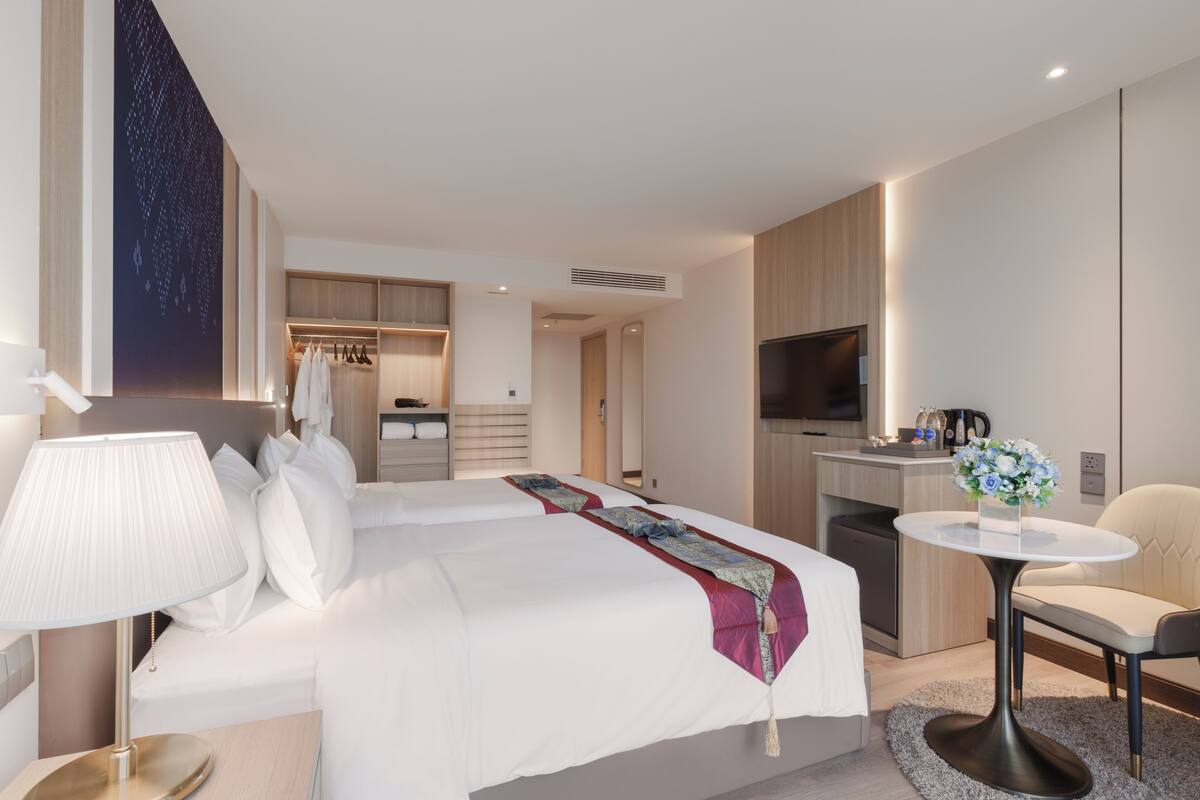 A hotel room with a bed, bedside table, lamp, TV, kitchenette, and a small dining area.