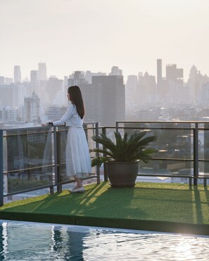 A person standing on a balcony with a cityscape view, a potted plant, and a pool. - SZ CANALSIDE HOTEL (Bangkok)
