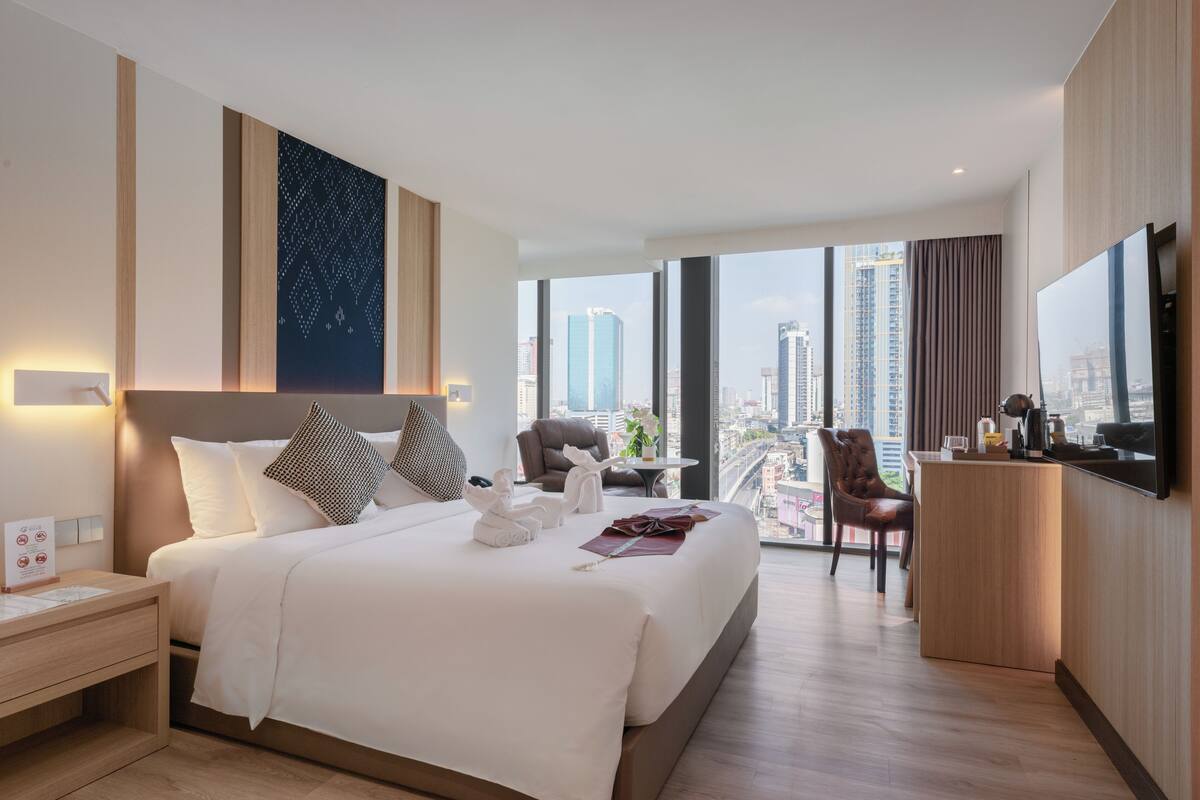 A modern hotel room with a large bed, a desk, a chair, and a city view.