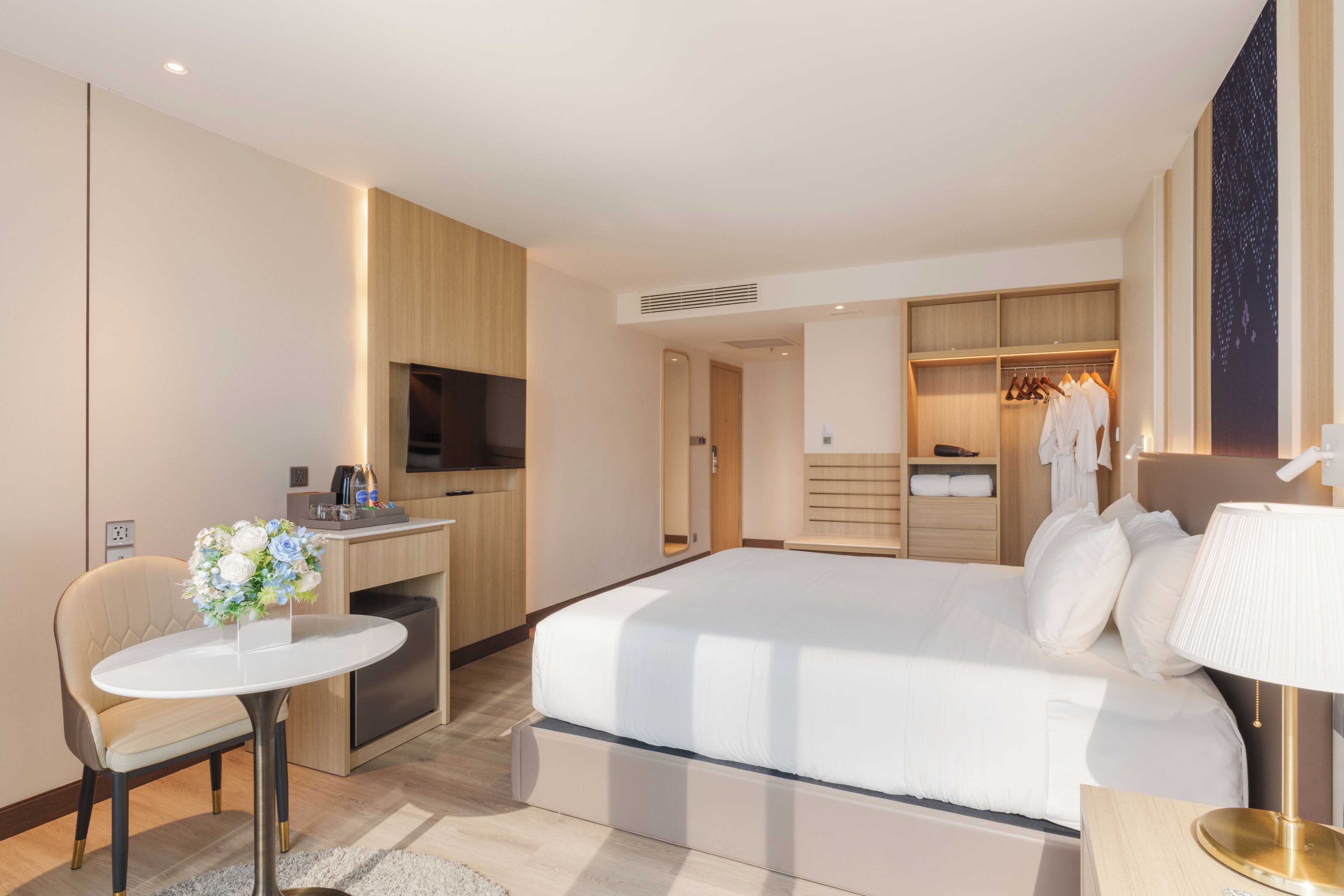 A modern hotel room with a bed, a desk, a chair, a TV, and a walk-in closet.