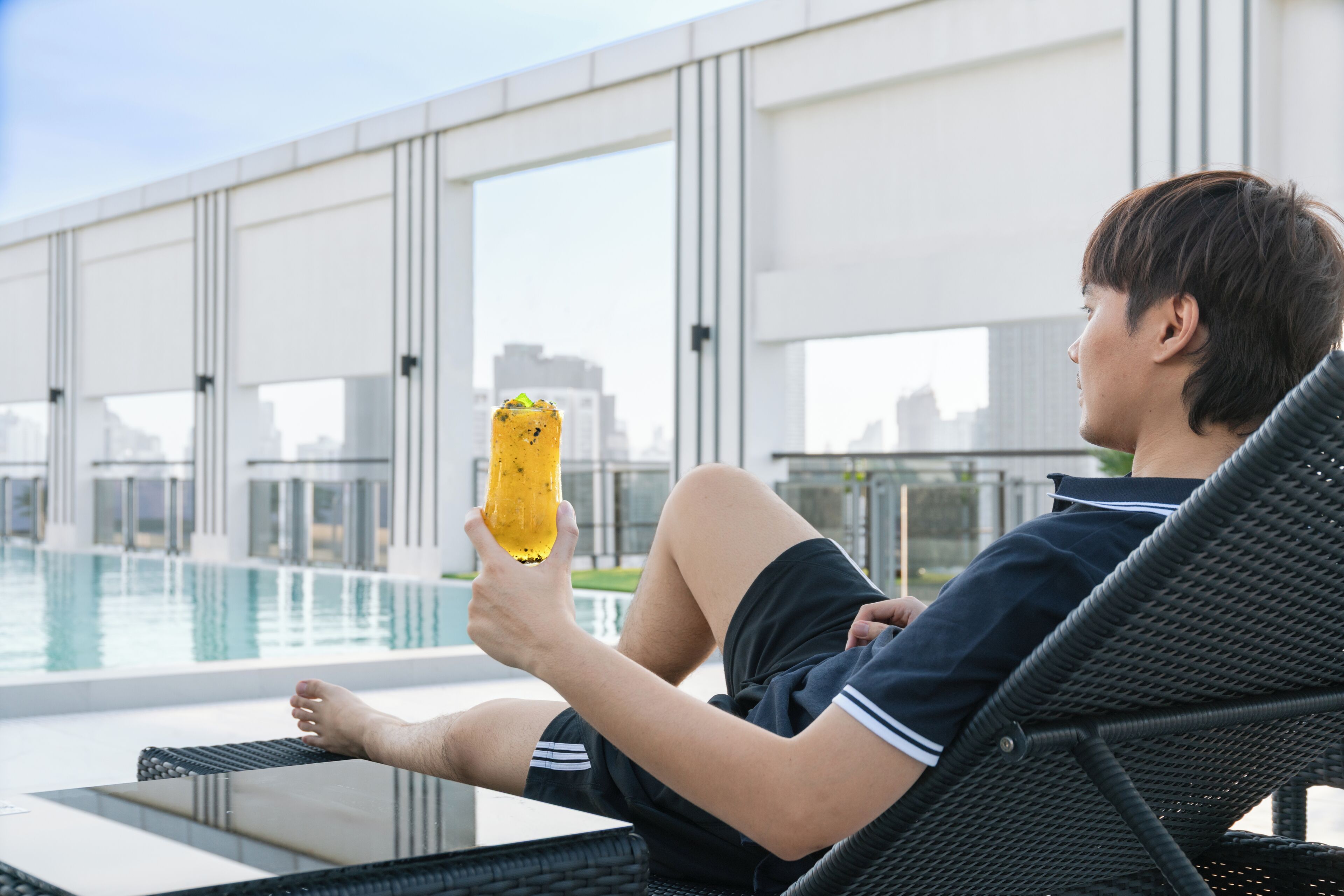 A person relaxing by a poolside lounge chair with a pool and modern architecture in the background.