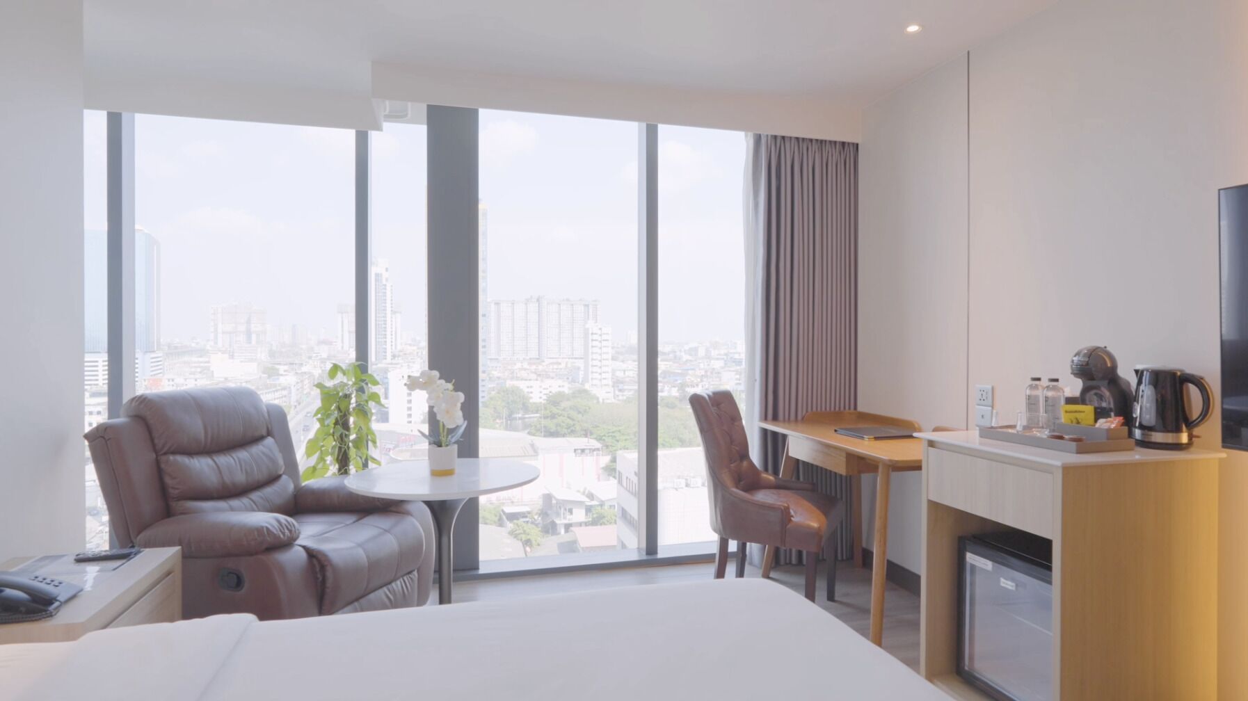 Ein Hotelzimmer mit einem großen Bett, einem Schreibtisch mit Stuhl, einer Kaffeemaschine und Blick auf die Stadt.