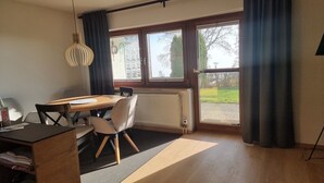 Quarto moderno com mesa de jantar, cadeiras, radiador e janelas amplas com cortinas.