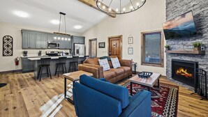 A spacious living area with a fireplace, a kitchen with grey cabinets, and a dining area with a wooden table and blue chairs. - Affordable AND Walk To the Strip, Hot Tub (Gatlinburg)