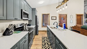 A modern kitchen with grey cabinets, a large island, and a stone accent wall. - Affordable AND Walk To the Strip, Hot Tub (Gatlinburg)