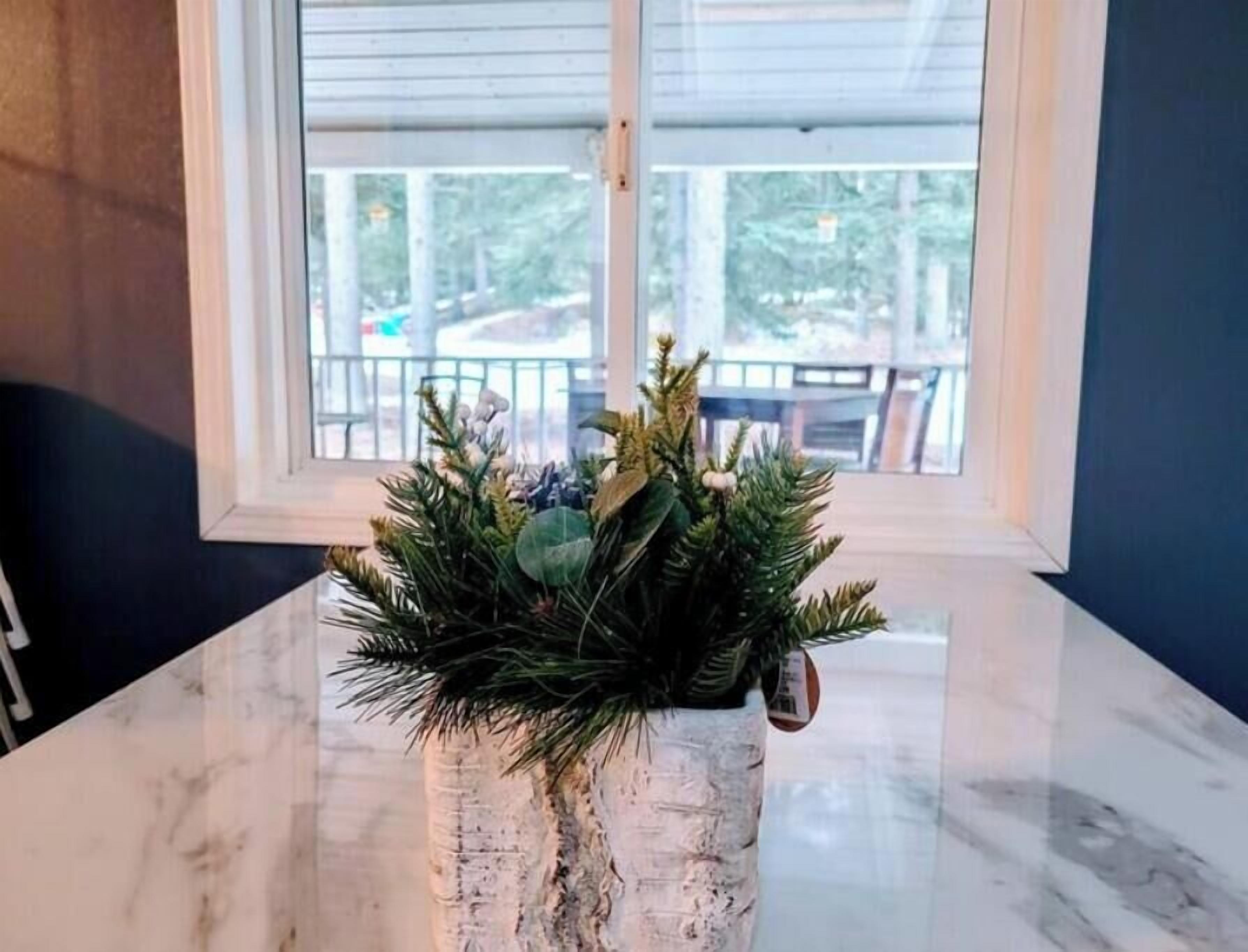 Una mesa de mármol con una maceta rústica y texturizada que contiene follaje verde y un adorno.