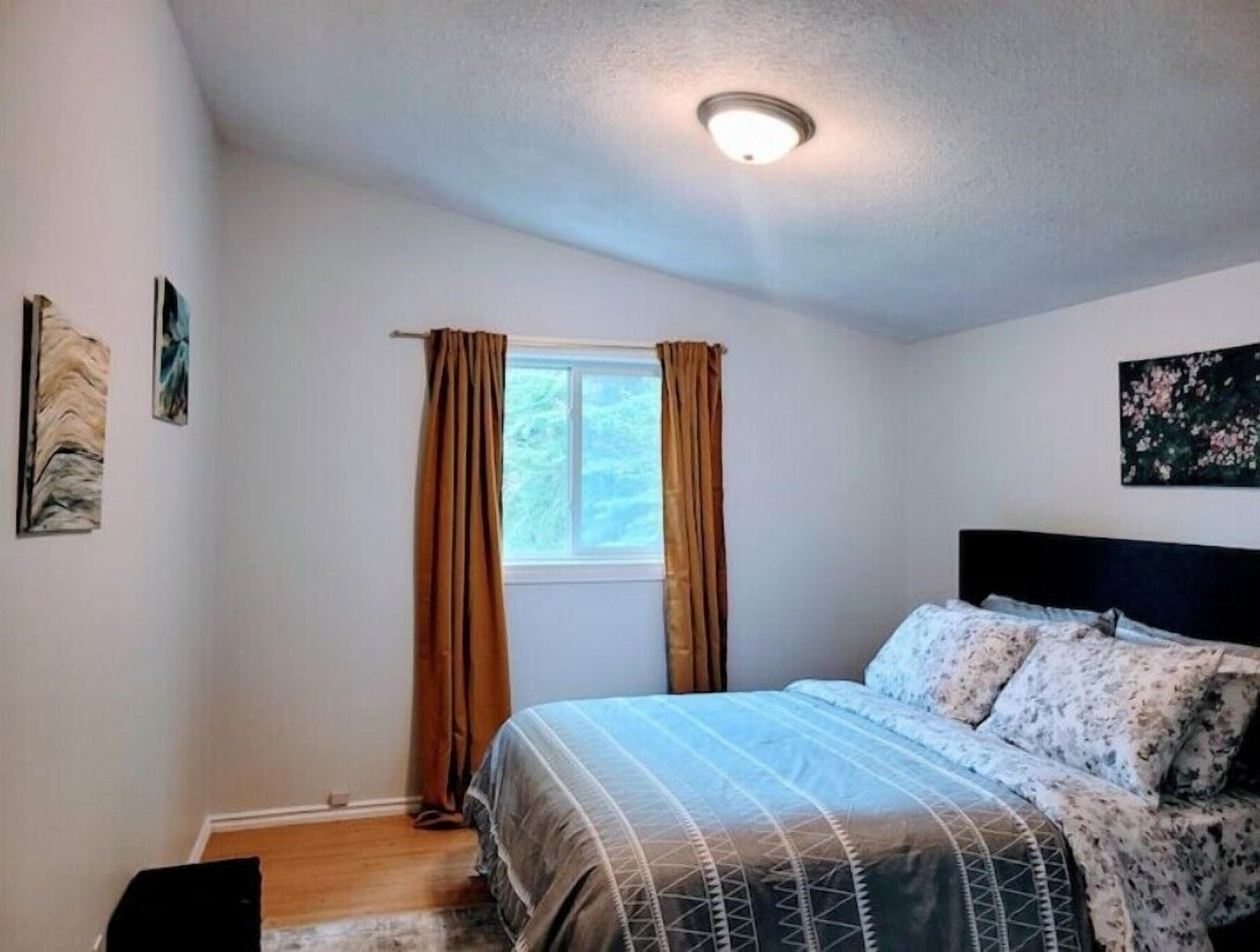 A bedroom with a bed, curtains, a window, and artwork on the walls.