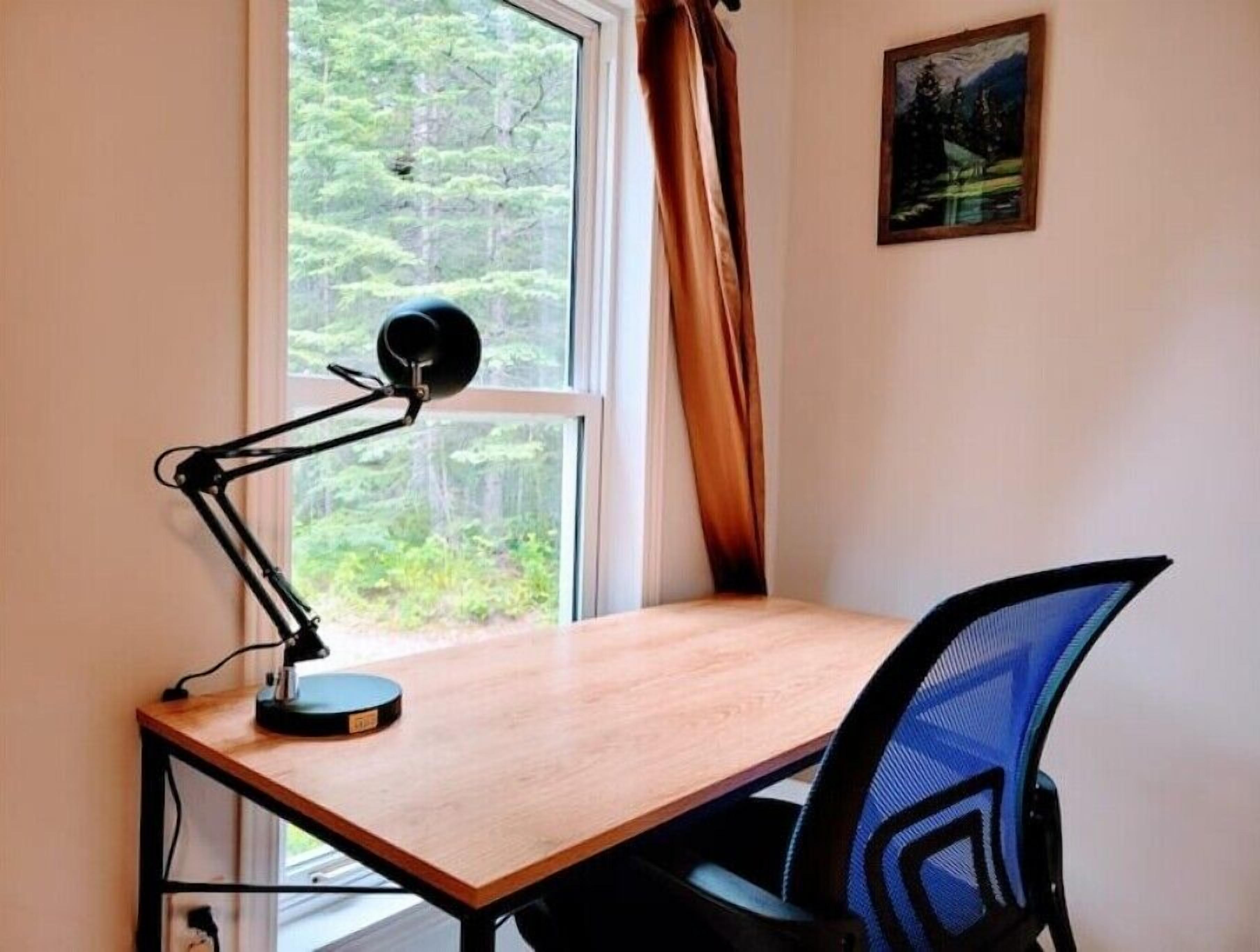 Une pièce comprenant un bureau, une chaise, une fenêtre avec un rideau et un tableau accroché au mur.