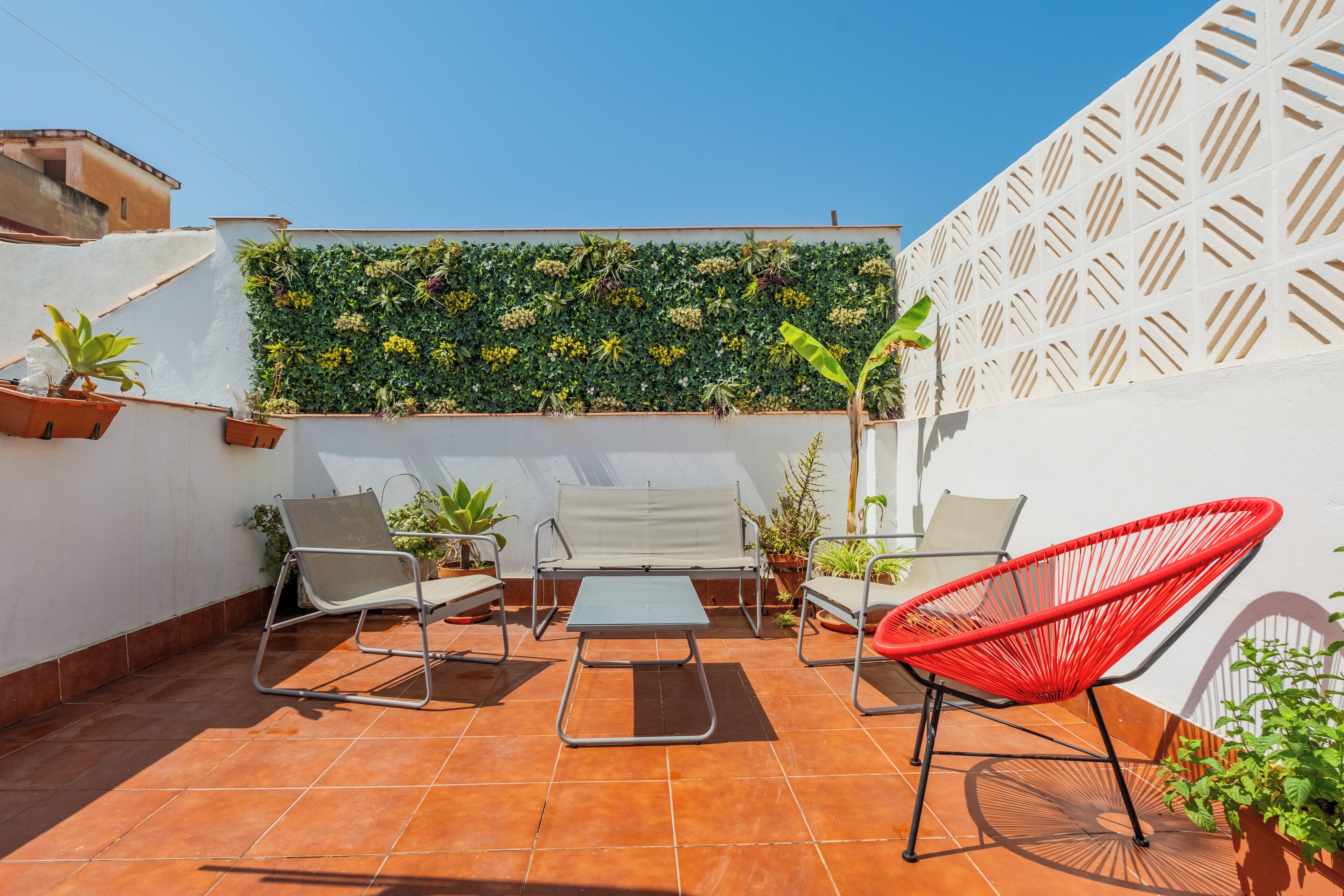 A patio with a white wall, a green vertical garden, and a red chair.