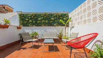 A patio with a white wall, a green vertical garden, and a red chair.