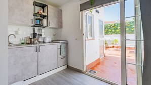 A modern kitchen with grey cabinets, a built-in shelf, and a view of the outdoor patio through a glass door. - Casita Lucero (Málaga)
